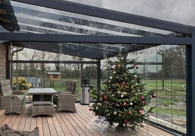 Terrassendach aus Aluminium mit Glasdach im Winter, geschützter Sitzbereich mit geschmücktem Weihnachtsbaum