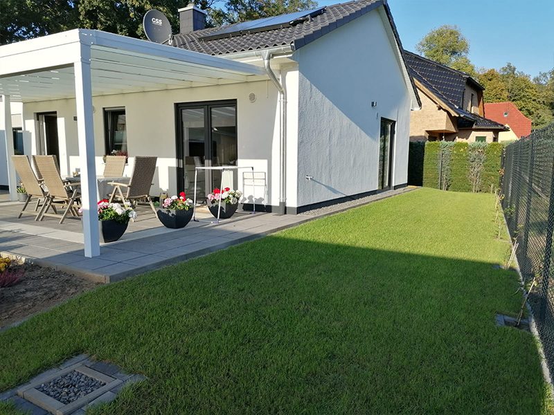 Weiße Terrassenüberdachung an einem Bungalow mit Rasenfläche